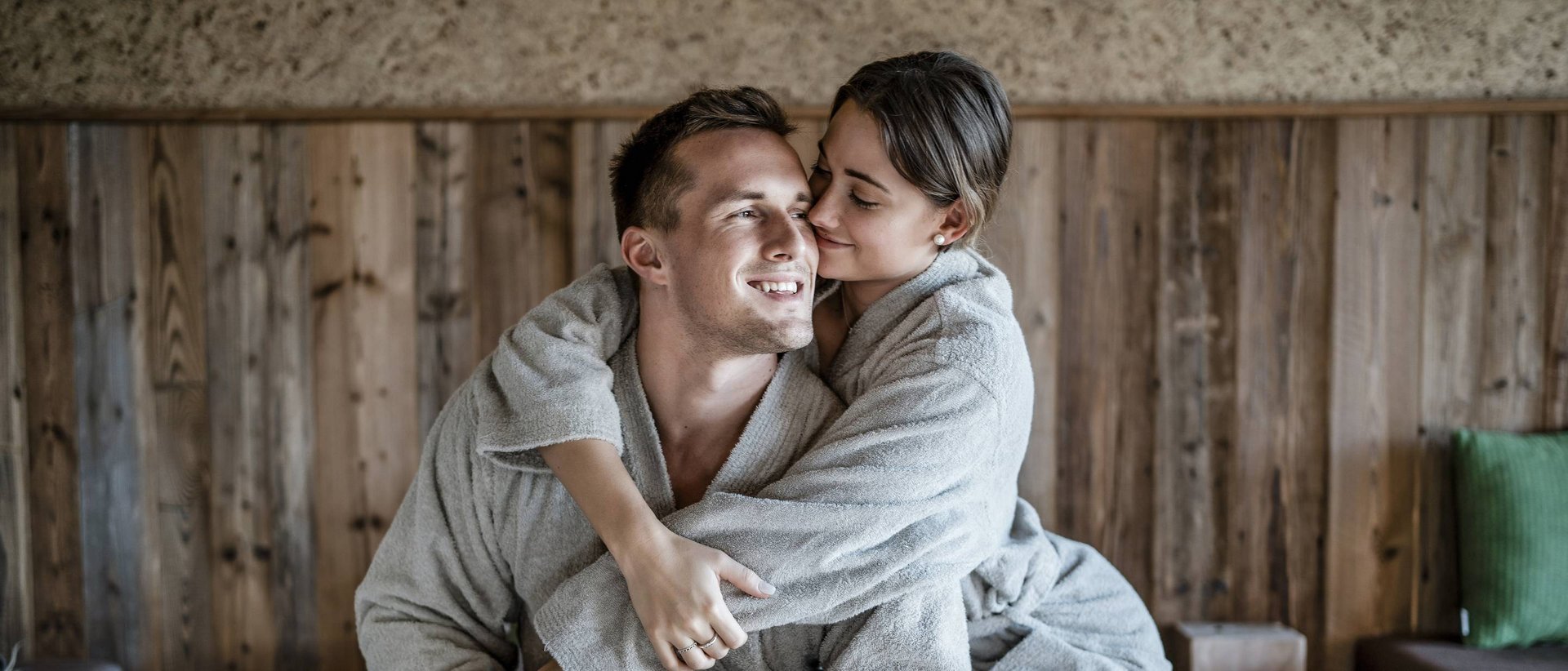 Hotel Weitblick Allgäu | Day SPA – Wellness für einen Tag Paar in grauen Bademänteln umarmt sich auf einem Bett in Holzzimmer